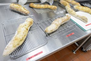 A variety of bread loafs made with different types of yeast are pulled from an oven during a FS 551: Fermented Food and Beverage class taught by Nick Smith, associate outreach specialist in the Department of Food Science at the University of Wisconsin-Madison, on April 25, 2018. The students in the course are helping to test the strains for suitability in bread baking, and are partnering with Clasen's Bakery in Middleton, Wisconsin to do so. (Photo by Bryce Richter / UW-Madison)