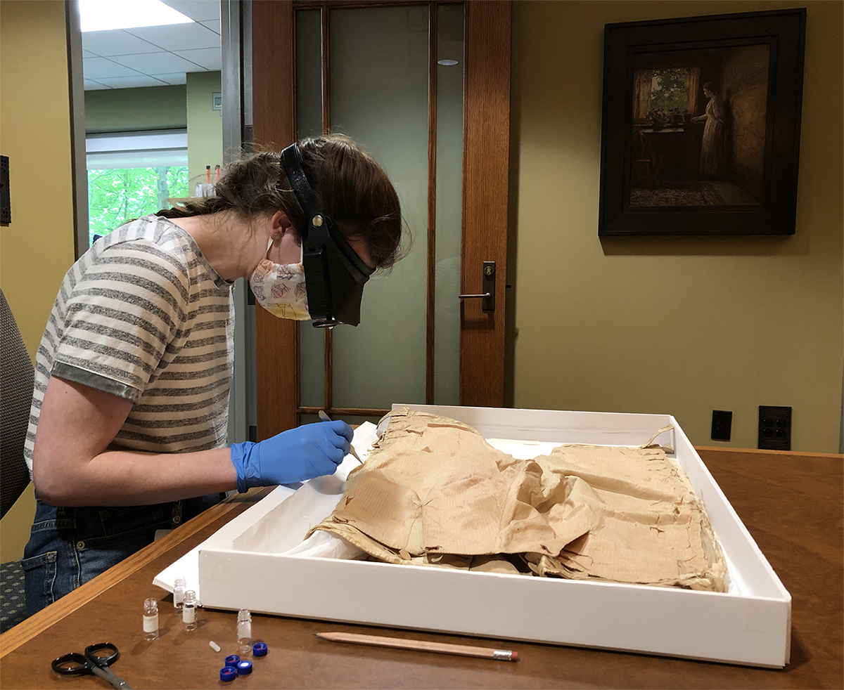 Erin Birdsall acquires samples from trousers. Tan trousers in white tray, test tubes off to side.